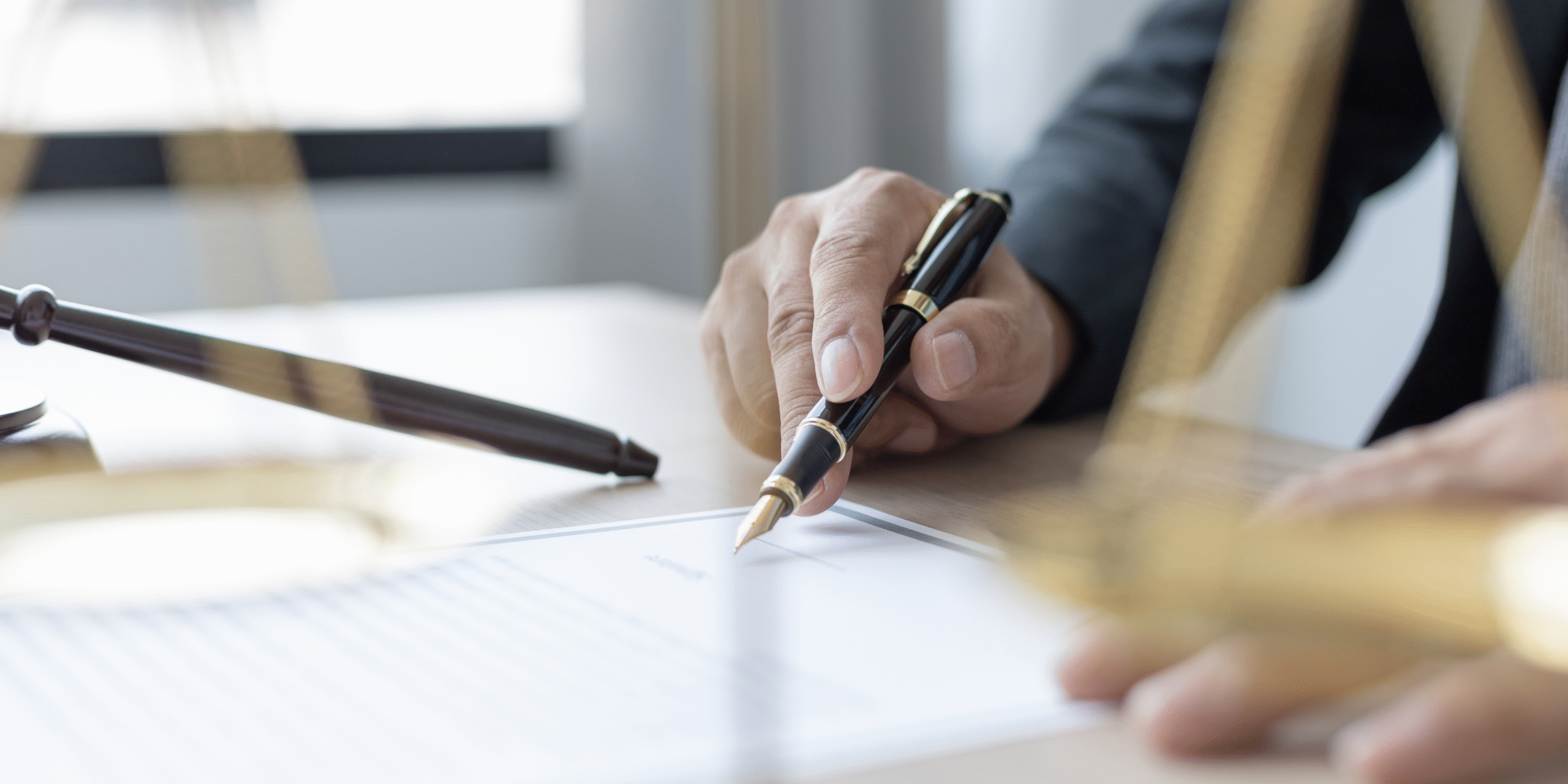 Un escritorio con un papel encima y una persona con una lapicera sobre el papel